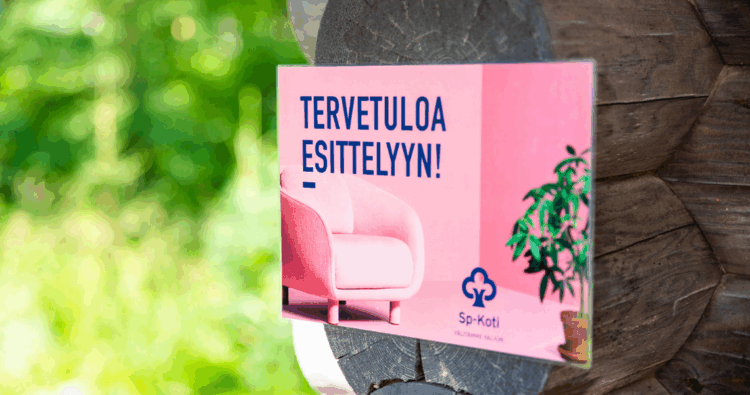 Vaaleanpunainen "Tervetuloa esittelyyn" kyltti kiinnitettynä hirren päähän.